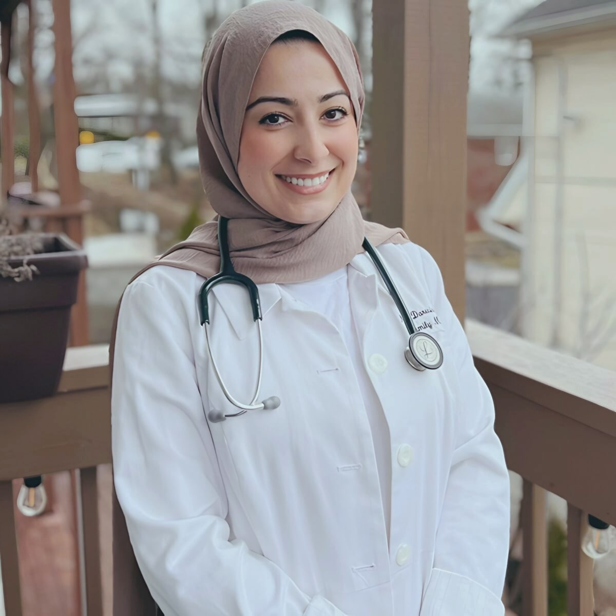Smiling woman doctor in hijab and white coat on porch
